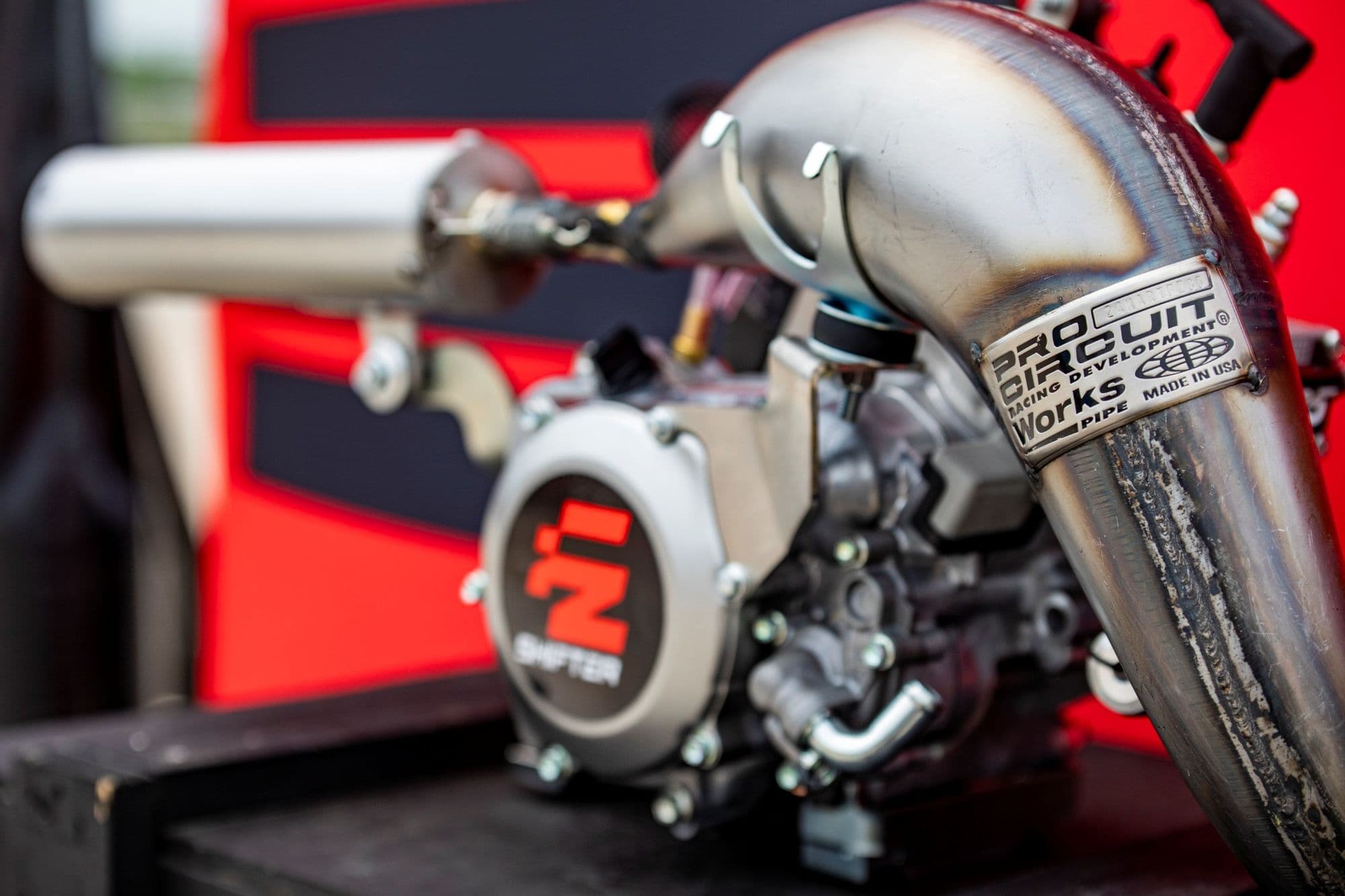 Close view of an FZ Shifter engine and exhaust on a red backdrop.